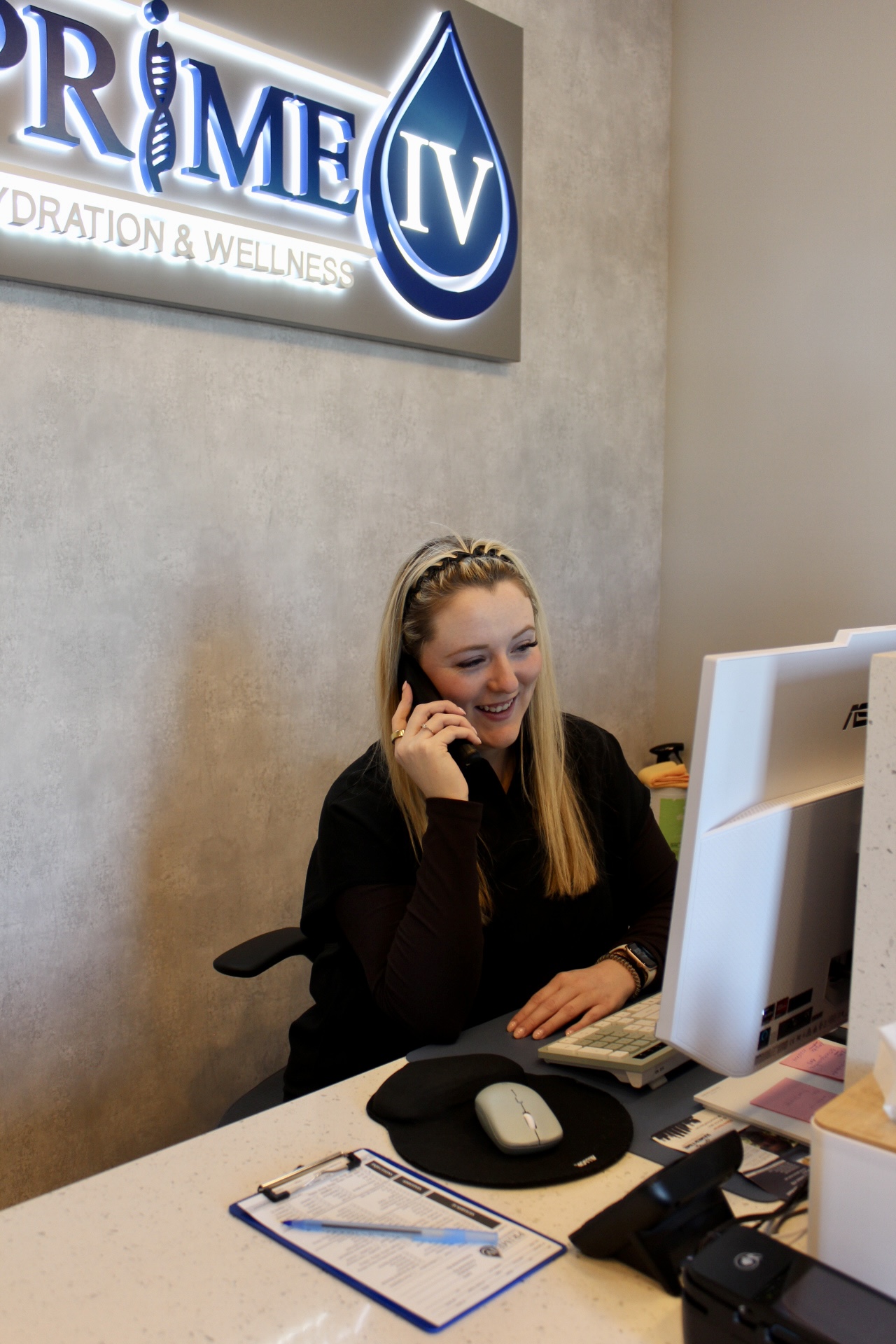 Friendly Prime IV Nolensville team member taking a call at the front desk beneath the illuminated Prime IV logo
